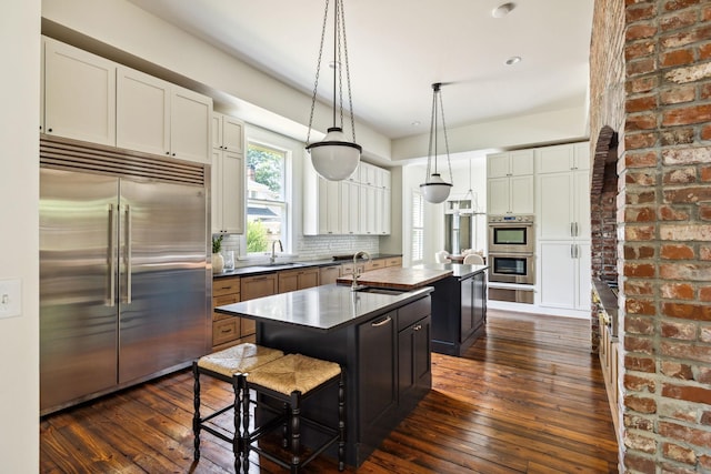 1051 W Main St, Franklin, TN 37064 - kitchen featuring appliances with stainless steel finishes, a kitchen island with sink, dark wood-type flooring, dark countertops, and a warming drawer