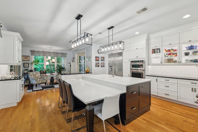 1313 Ridge Rd, Dickson, TN 37055 - kitchen featuring stainless steel appliances, a center island with sink, white cabinetry, hanging light fixtures, and light wood finished floors