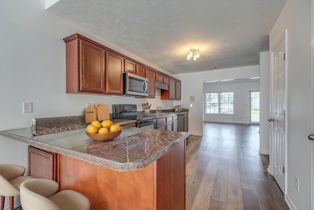 2026 Caladonia Way, Smyrna, TN 37167 - kitchen featuring black electric range oven, stainless steel microwave, a breakfast bar, brown cabinetry, and a peninsula