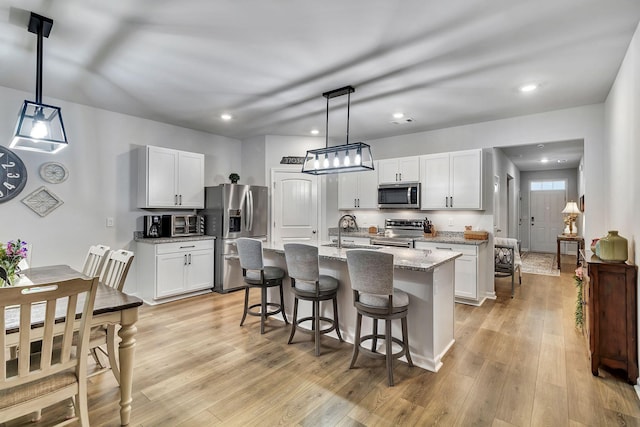 211 Addison Ave, Chapel Hill, TN 37034 - kitchen featuring appliances with stainless steel finishes, a kitchen island with sink, a kitchen bar, light wood-style flooring, and white cabinets