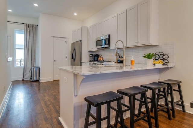 2001 Convent Pl Unit 7, Nashville, TN 37212 - kitchen with appliances with stainless steel finishes, a peninsula, tasteful backsplash, light stone countertops, and dark wood-type flooring
