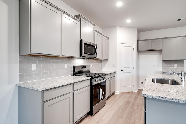 316 Deacon Ln, White House, TN 37188 - kitchen featuring appliances with stainless steel finishes, gray cabinetry, a sink, light wood-style flooring, and backsplash