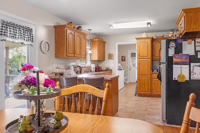 4190 Tanyard Hill Rd, Lynchburg, TN 37352 - kitchen with freestanding refrigerator, a peninsula, washer / dryer, and brown cabinetry
