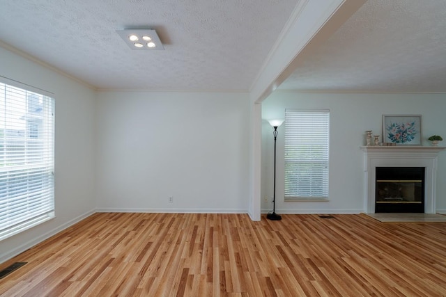 405 Parish Pl, Franklin, TN 37067 - unfurnished living room featuring a textured ceiling, crown molding, light wood-style flooring, healthy amount of natural light, and a glass covered fireplace