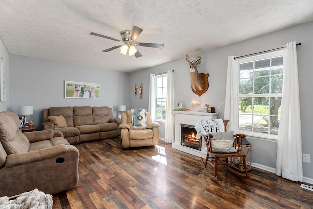 5024 Short Mountain Hwy, Smithville, TN 37166 - living area featuring dark wood-type flooring, a textured ceiling, a ceiling fan, a warm lit fireplace, and baseboards