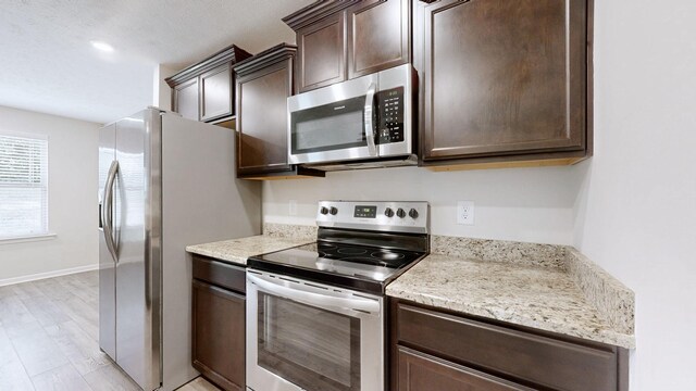 249 Edgefield Ct, Pleasant View, TN 37146 - kitchen with stainless steel appliances, dark brown cabinetry, light wood-type flooring, and light stone countertops