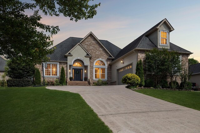 7579 Nightfall Cir, Ooltewah, TN 37363 - french country home with an attached garage, a front yard, concrete driveway, brick siding, and a shingled roof