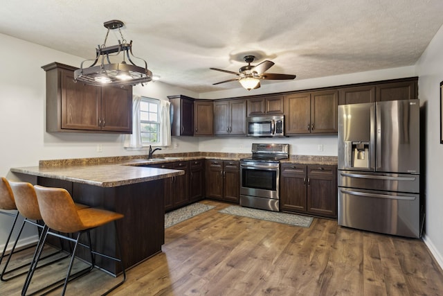 4010 Swift Springs Ct, Goodlettsville, TN 37072 - kitchen with appliances with stainless steel finishes, a peninsula, dark brown cabinets, a sink, and dark wood-style flooring