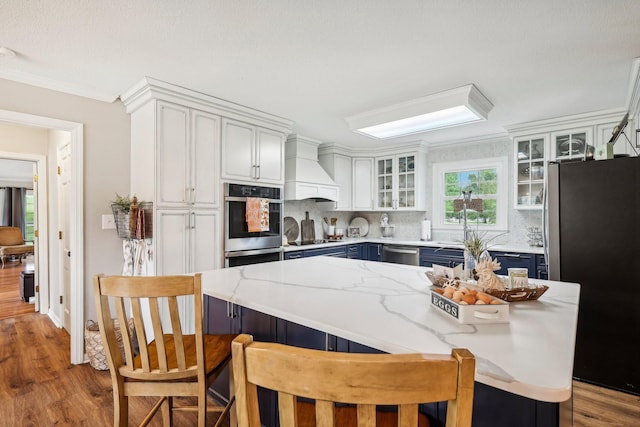 3411 Murphy Ln, Columbia, TN 38401 - kitchen with stainless steel appliances, custom range hood, wood finished floors, blue cabinetry, and tasteful backsplash