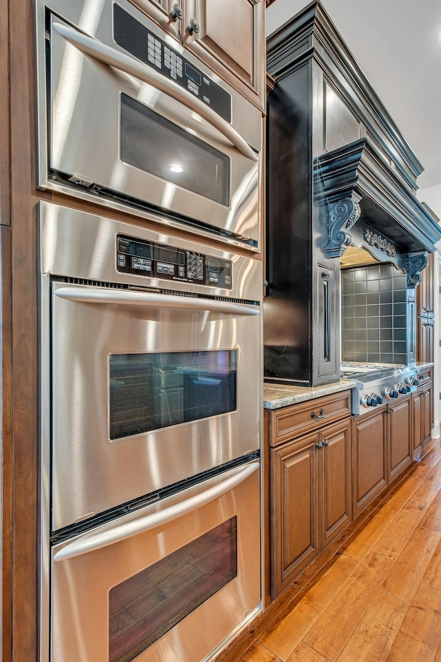 1120 Natchez Valley Ln, Franklin, TN 37064 - kitchen featuring stainless steel appliances, brown cabinets, light wood-style floors, and light stone counters