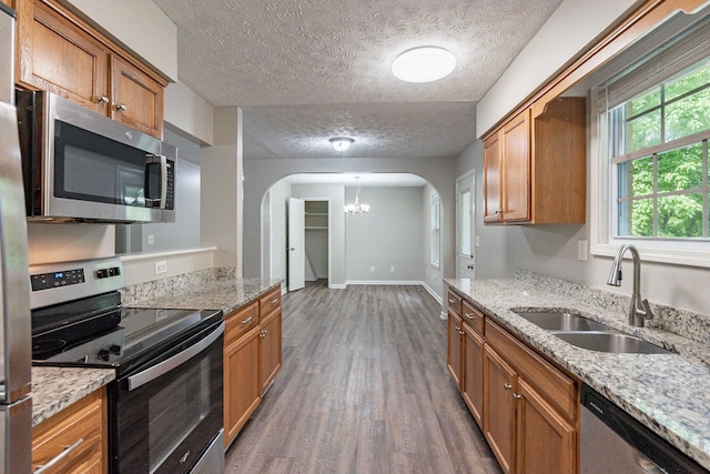 104 Evanmeade Dr, Smyrna, TN 37167 - kitchen featuring stainless steel appliances, arched walkways, brown cabinetry, dark wood-style floors, and a sink