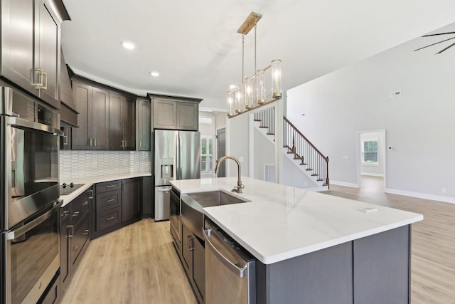 1373 Southside Rd, Southside, TN 37171 - kitchen featuring appliances with stainless steel finishes, light wood-style floors, backsplash, a center island with sink, and hanging light fixtures