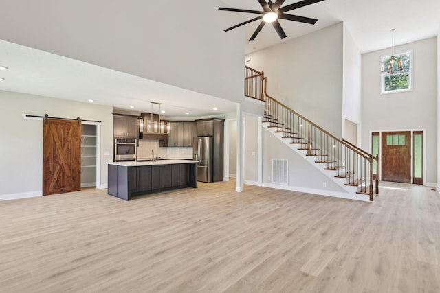 1373 Southside Rd, Southside, TN 37171 - unfurnished living room featuring a barn door, a high ceiling, light wood-type flooring, stairway, and a chandelier