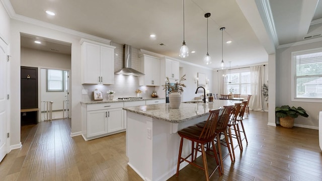 6614 Floral Ct, Murfreesboro, TN 37128 - kitchen featuring wall chimney exhaust hood, stainless steel gas cooktop, ornamental molding, an island with sink, and a sink