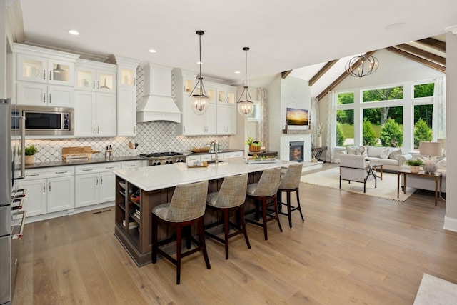 7243 Murrel Dr, Franklin, TN 37064 - kitchen featuring custom exhaust hood, stainless steel microwave, backsplash, white cabinetry, and a breakfast bar area