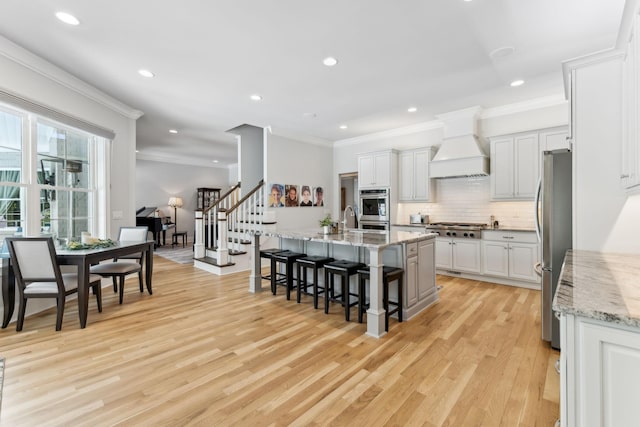 4043 Old Light Cir, Arrington, TN 37014 - kitchen with premium range hood, stainless steel appliances, a kitchen breakfast bar, light wood-style floors, and tasteful backsplash