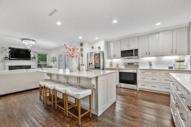 814 Riata Ct, Smyrna, TN 37167 - kitchen with appliances with stainless steel finishes, light countertops, open floor plan, white cabinetry, and a kitchen bar