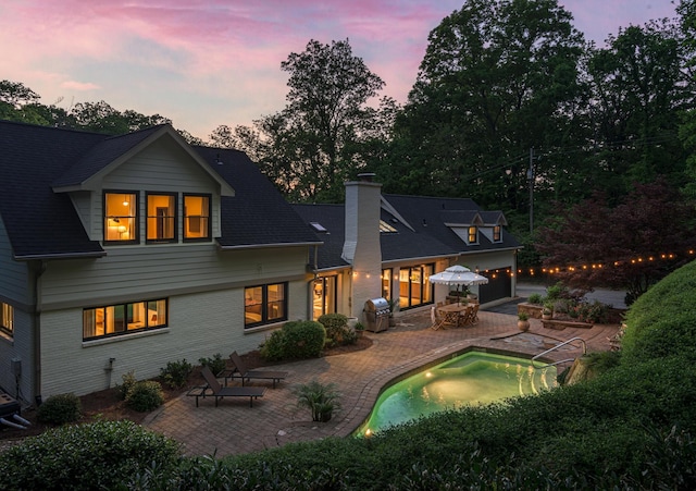 2300 Chickering Ln, Nashville, TN 37215 - back of house at dusk featuring a patio, a chimney, a garage, an outdoor pool, and brick siding