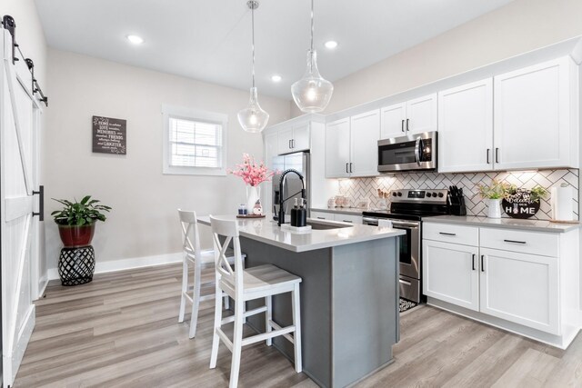 207 Charleston Ave, Pleasant View, TN 37146 - kitchen featuring appliances with stainless steel finishes, decorative backsplash, white cabinetry, light wood-style floors, and a breakfast bar area