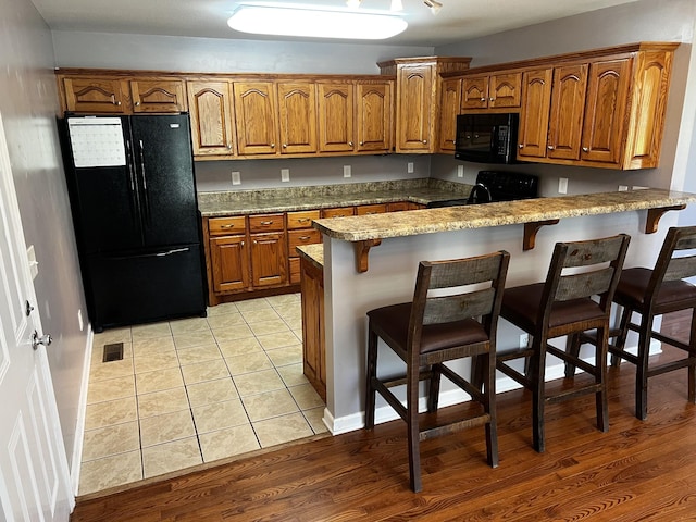 168 Commodore Cir, Summertown, TN 38483 - kitchen featuring black appliances, brown cabinetry, a peninsula, a kitchen bar, and light tile patterned floors