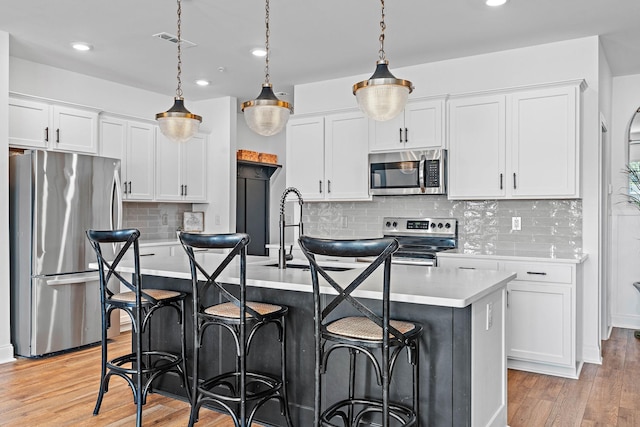 1246 June Wilde Rdg, Spring Hill, TN 37174 - kitchen featuring stainless steel appliances, light countertops, light wood finished floors, an island with sink, and white cabinetry