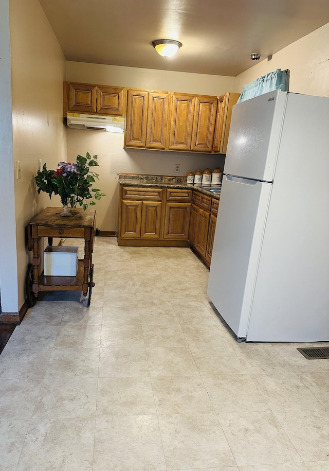915 Wedgewood Ave, Nashville, TN 37203 - kitchen featuring freestanding refrigerator, brown cabinets, under cabinet range hood, dark countertops, and baseboards