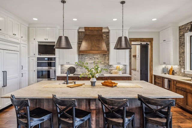 3166 Tanyard Hollow Rd, Culleoka, TN 38451 - kitchen with double oven, premium range hood, decorative backsplash, a center island with sink, and dark wood finished floors