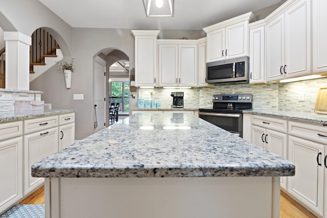 6288 Blacksmith Dr, Pleasant View, TN 37146 - kitchen with stainless steel appliances, arched walkways, a kitchen island, light stone counters, and light wood-type flooring