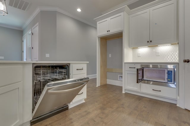 7137 Frances St, Fairview, TN 37062 - kitchen with ornamental molding, stainless steel microwave, wood finished floors, decorative backsplash, and white cabinetry