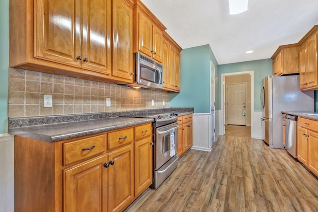 2137 Horton Way, Lewisburg, TN 37091 - kitchen with stainless steel appliances, light wood-style floors, brown cabinets, a wainscoted wall, and dark countertops