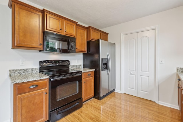 2889 Sharpie Dr, Clarksville, TN 37040 - kitchen with black appliances, light wood-style floors, brown cabinetry, light stone counters, and baseboards