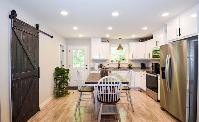 421 Marlin Ln, Westmoreland, TN 37186 - kitchen featuring stainless steel appliances, a barn door, white cabinets, light wood-style flooring, and decorative light fixtures