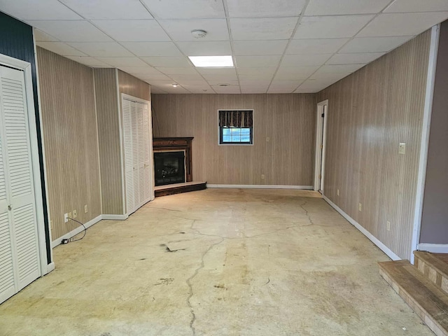 102 Hazelnut Ave, Camden, TN 38320 - unfurnished living room featuring concrete flooring, a fireplace with raised hearth, wooden walls, a paneled ceiling, and baseboards