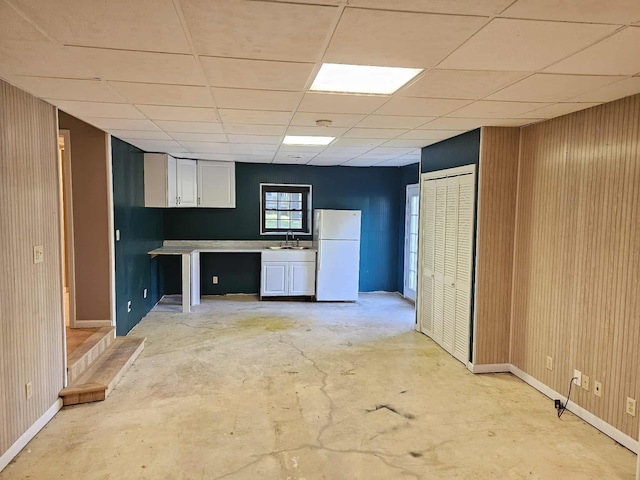 102 Hazelnut Ave, Camden, TN 38320 - kitchen with freestanding refrigerator, baseboards, white cabinets, wood walls, and unfinished concrete floors