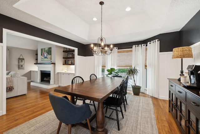 519 Glen Echo Dr, Old Hickory, TN 37138 - dining space with a chandelier, light wood-style flooring, a fireplace with raised hearth, a raised ceiling, and a wainscoted wall