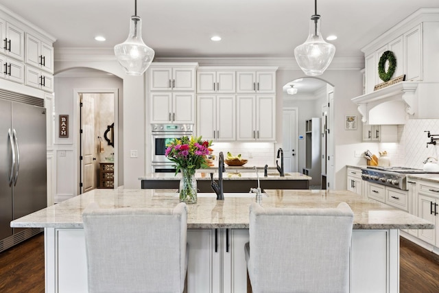 1234 Saddle Springs Dr, Thompsons Station, TN 37179 - kitchen featuring appliances with stainless steel finishes, arched walkways, a kitchen island with sink, ornamental molding, and tasteful backsplash