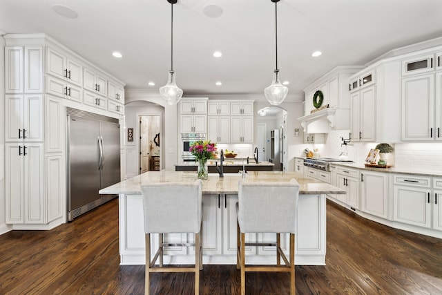 1234 Saddle Springs Dr, Thompsons Station, TN 37179 - kitchen featuring appliances with stainless steel finishes, arched walkways, a center island with sink, white cabinets, and decorative backsplash