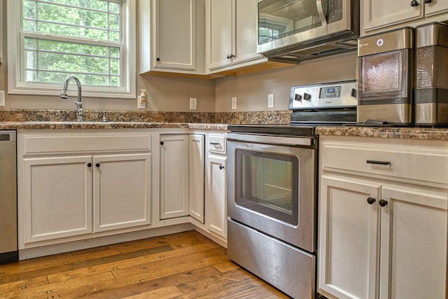 143 Rachelle Pl, Baxter, TN 38544 - kitchen featuring appliances with stainless steel finishes, a sink, light wood-style floors, dark stone counters, and white cabinetry