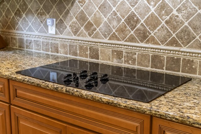 9166 Sydney Ln, Brentwood, TN 37027 - kitchen view of black electric stovetop, decorative backsplash, brown cabinets, and light stone counters