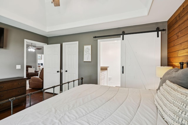 2754 Douglas Ln, Thompsons Station, TN 37179 - bedroom with a barn door, wood finished floors, a tray ceiling, connected bathroom, and wood walls
