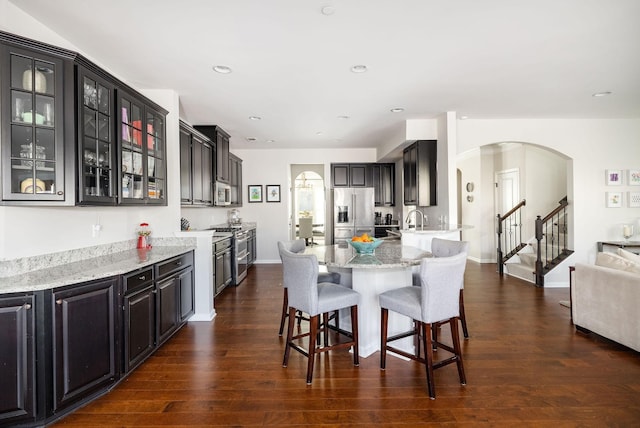 6050 Huntmere Ave, Franklin, TN 37064 - kitchen featuring stainless steel appliances, arched walkways, a breakfast bar, light stone countertops, and dark wood-type flooring