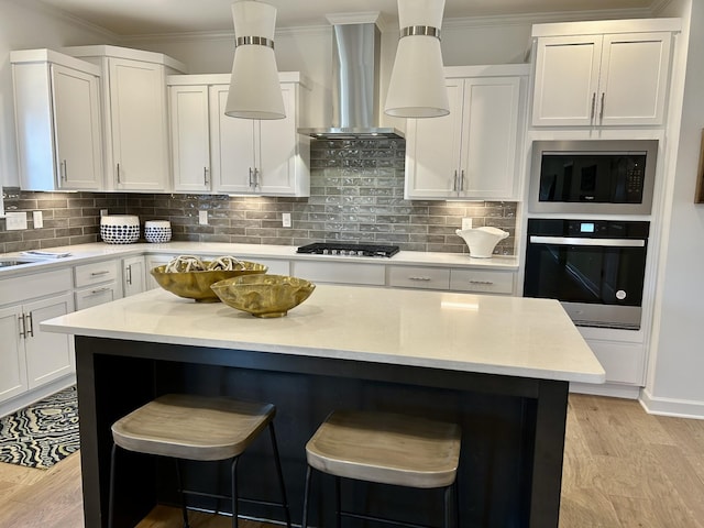 6705 Major Hutchings Dr, Hermitage, TN 37076 - kitchen with stainless steel appliances, wall chimney range hood, a kitchen breakfast bar, white cabinetry, and light wood finished floors