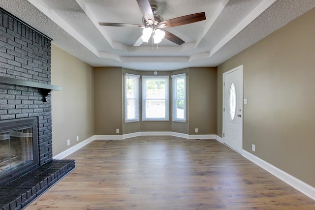 1783 Forrestdale Dr, Clarksville, TN 37042 - unfurnished living room featuring a tray ceiling, wood finished floors, a brick fireplace, ceiling fan, and a textured ceiling