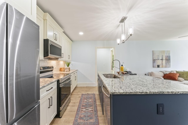 712 N 5th St, Nashville, TN 37207 - kitchen featuring appliances with stainless steel finishes, a sink, light wood finished floors, decorative backsplash, and a kitchen island with sink