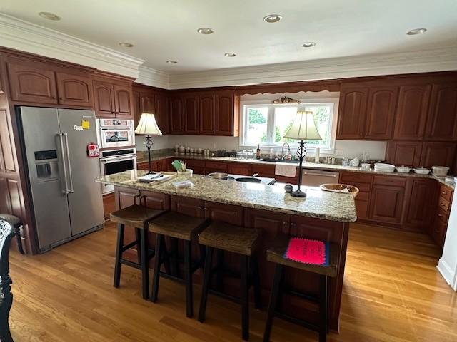 106 Rigney Rd, Manchester, TN 37355 - kitchen featuring appliances with stainless steel finishes, a center island with sink, a breakfast bar, ornamental molding, and light wood-type flooring