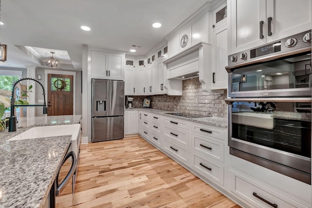 2670 Morgan Rd, Joelton, TN 37080 - kitchen featuring appliances with stainless steel finishes, white cabinetry, light wood finished floors, tasteful backsplash, and glass insert cabinets