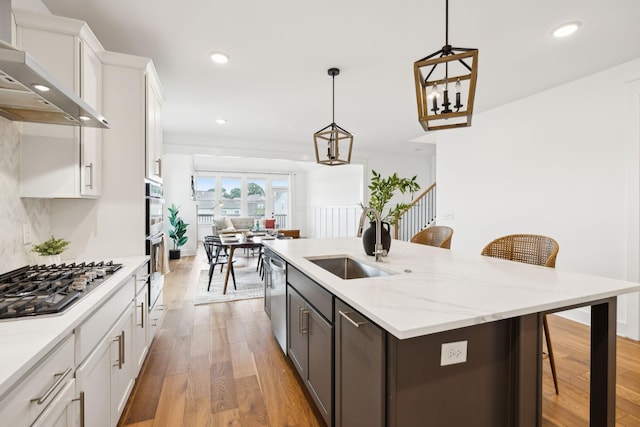 3298 Vinemont Dr, Thompsons Station, TN 37179 - kitchen with wall chimney exhaust hood, stainless steel appliances, a sink, light wood-style flooring, and a breakfast bar