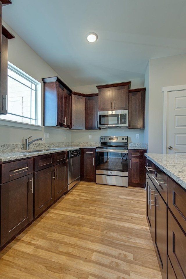 3010 Coriander Dr, Spring Hill, TN 37174 - kitchen featuring stainless steel appliances, light wood-style floors, dark brown cabinetry, light stone counters, and a sink