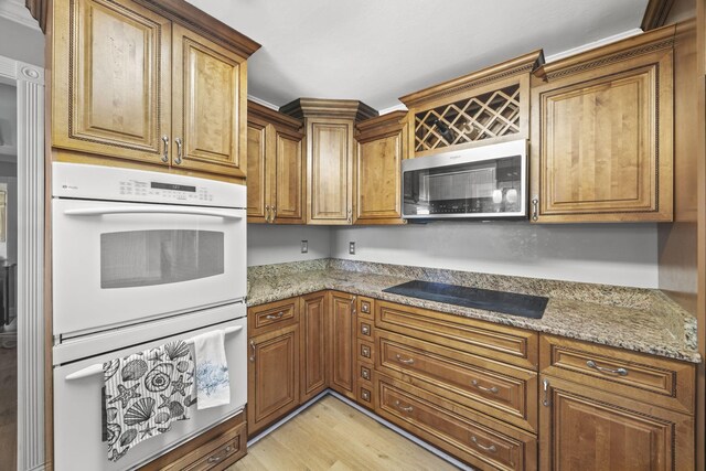 255 Whispering Hills Dr, Dover, TN 37058 - kitchen with stainless steel microwave, black electric stovetop, white double oven, brown cabinetry, and light wood-type flooring