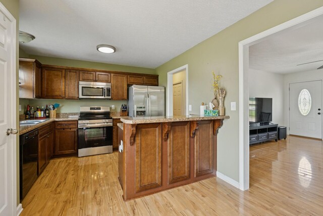 1809 Mosley Ferry Rd, Chapmansboro, TN 37035 - kitchen featuring stainless steel appliances, light wood finished floors, light stone counters, a peninsula, and a breakfast bar